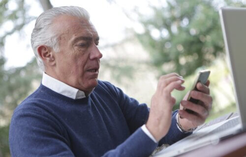older man on smartphone in front of laptop