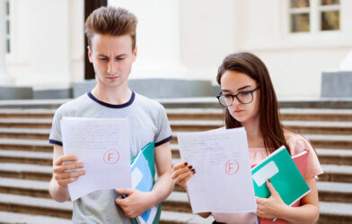 Sad students holding papers with bad results of test