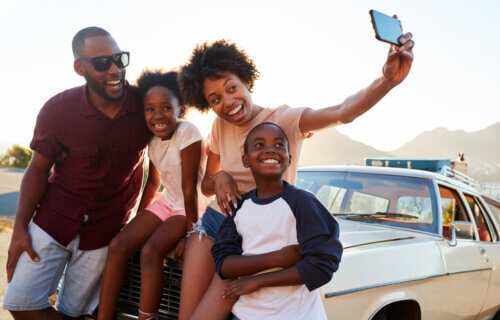 Family road trip: Parents take selfie with kids in front of car