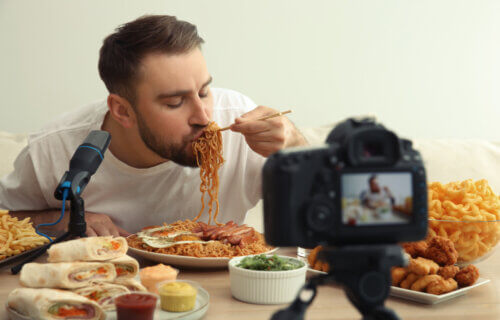 Mukbang video host slurps noodles amid plates of other unhealthy foods.