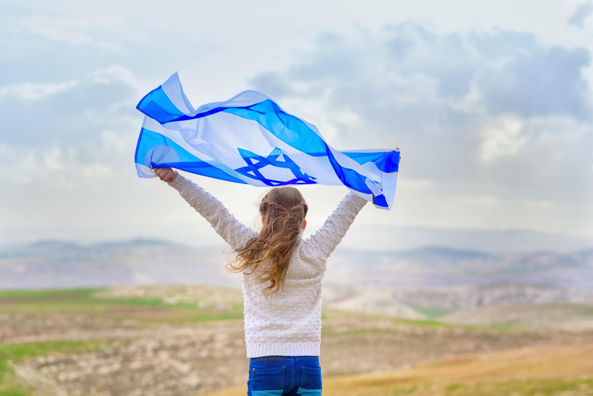 Young Jewish girl raising an Israeli flag in the air. 