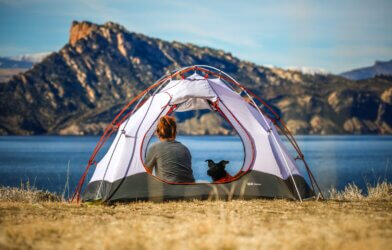 A woman and her dog sitting in a tent by a mountain and lake