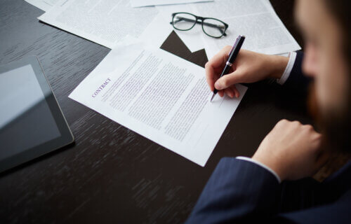 Image of businessman hand with pen signing contract at workplace