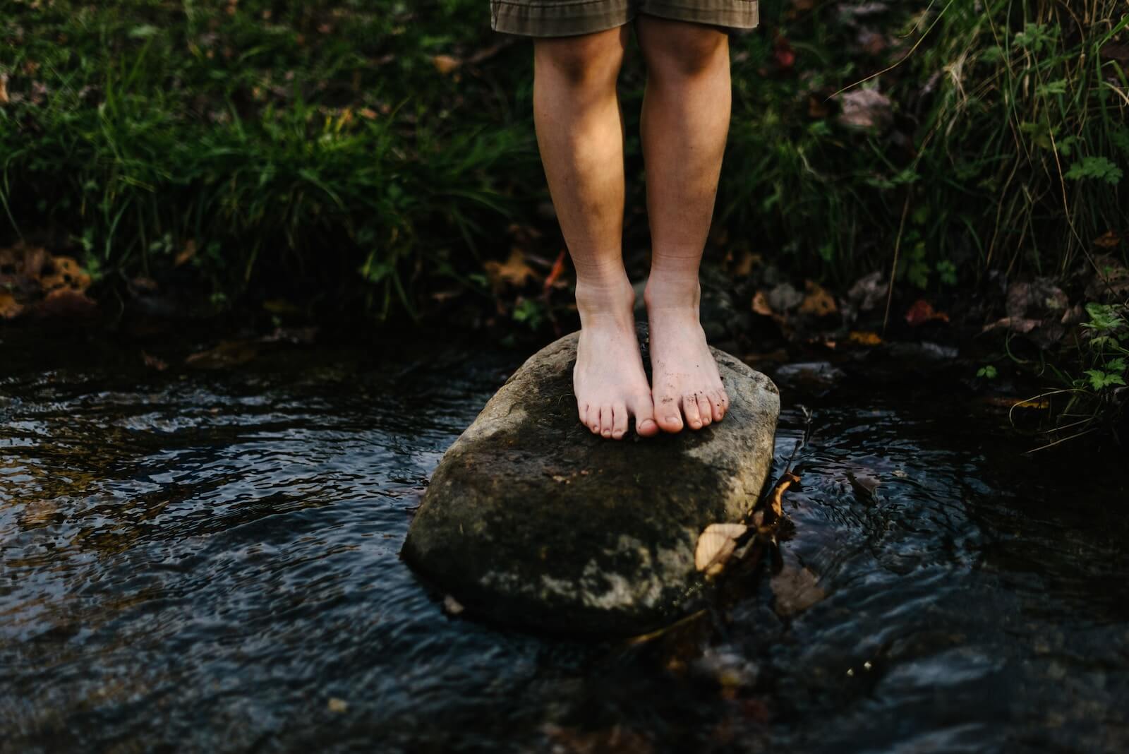 Person barefoot on a rock in a stream