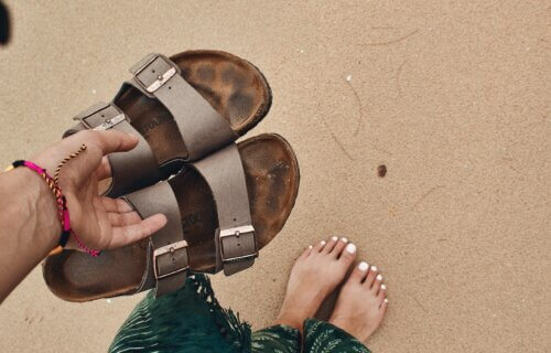 Someone holding a pair of Birkenstock sandals on the beach