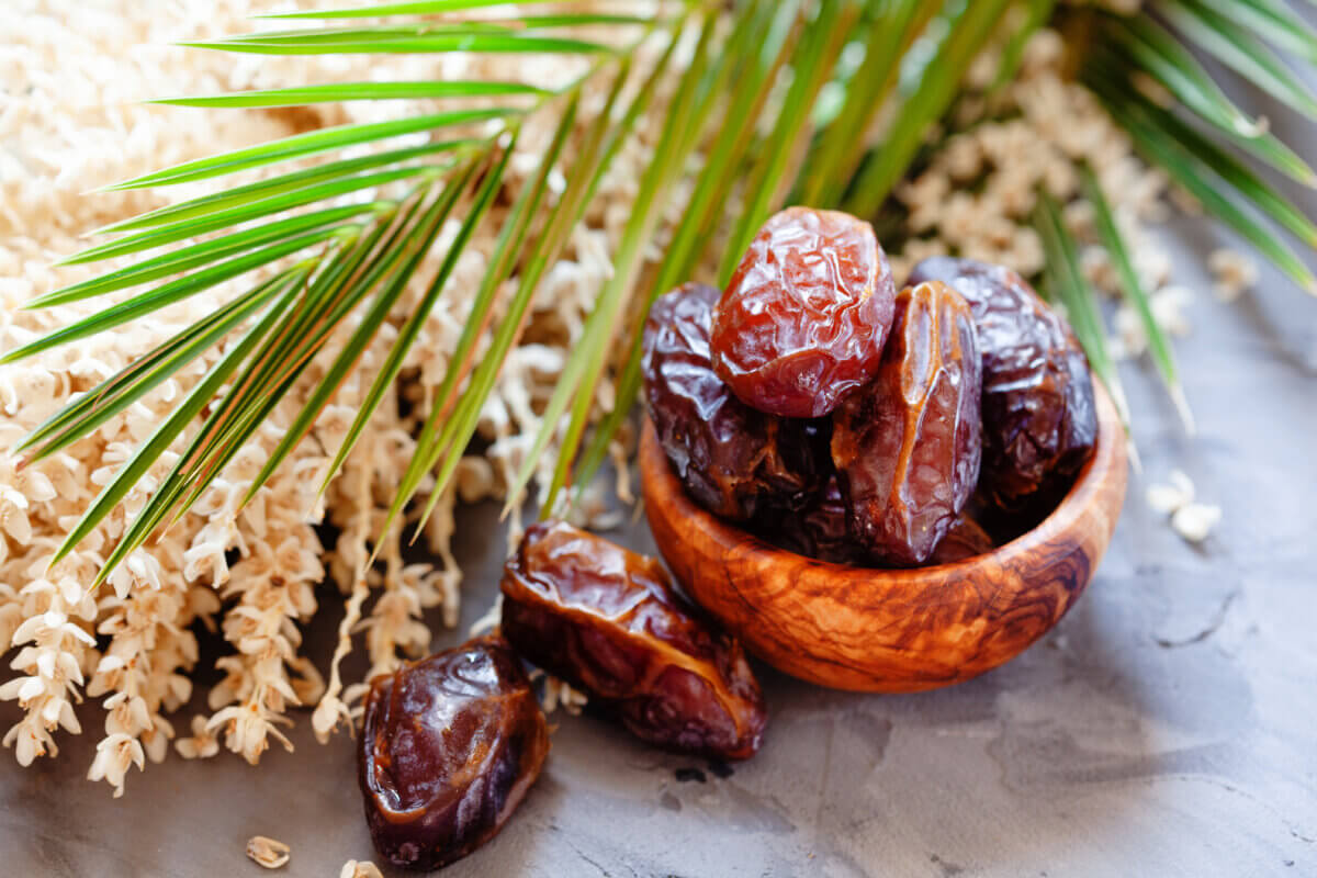Bowl of raw organic medjool dates with leaves and flowers of date palm