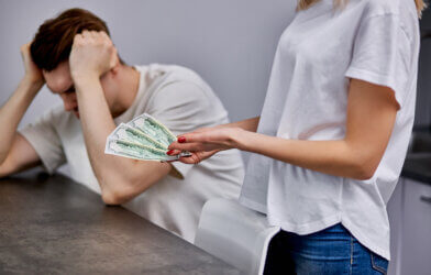 young wife holding money next to dissatisfied husband