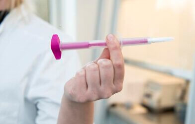 close up picture of a hand of person wearing a white jacket, holding up a pink plastic stick with a white tube
