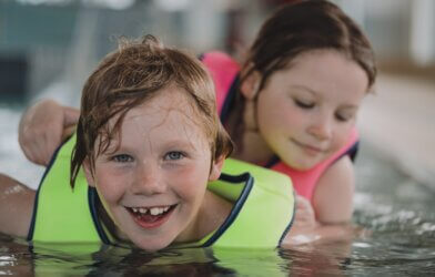 Two kids in a pool with life vests