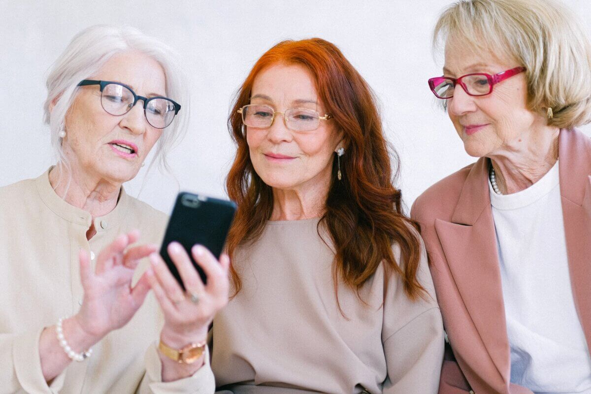 Happy aged women in eyeglasses looking at screen of smartphone