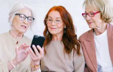 Happy aged women in eyeglasses looking at screen of smartphone