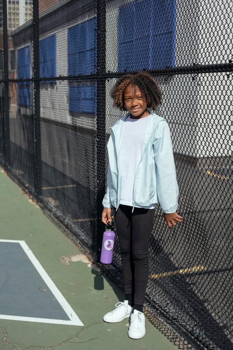 A young girl holding a water bottle on a tennis court