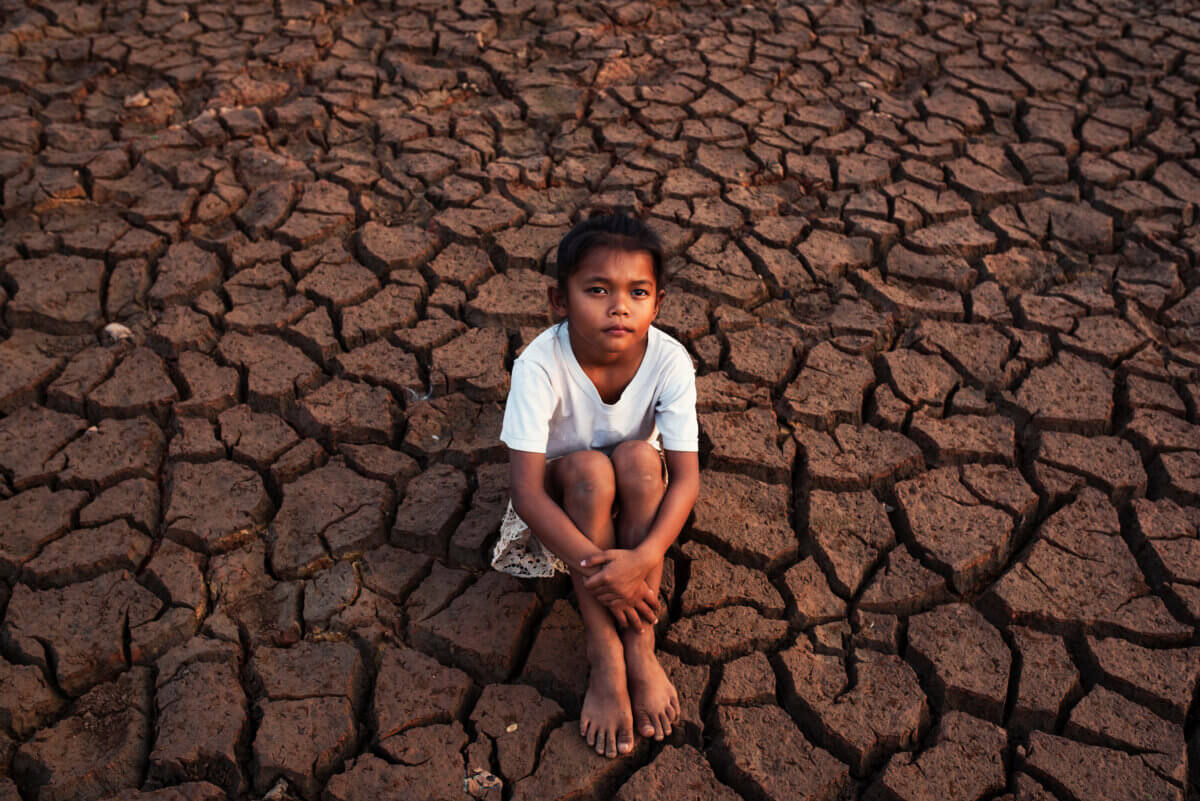 A poor child sits on dry ground during drought 