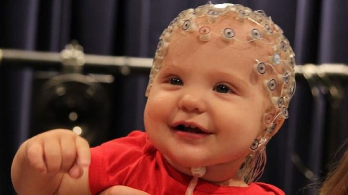 smiling baby in a red shirt with multiple electrodes attached to the scalp