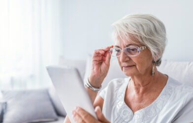 Older woman looking at a tablet or smartphone while fixing her reading glases