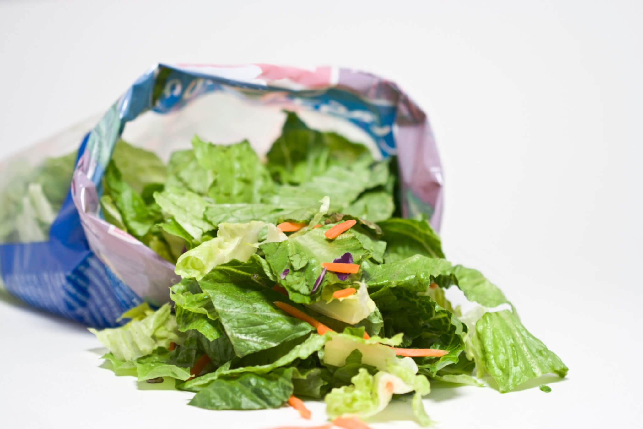 Open bag of salad with lettuce on table