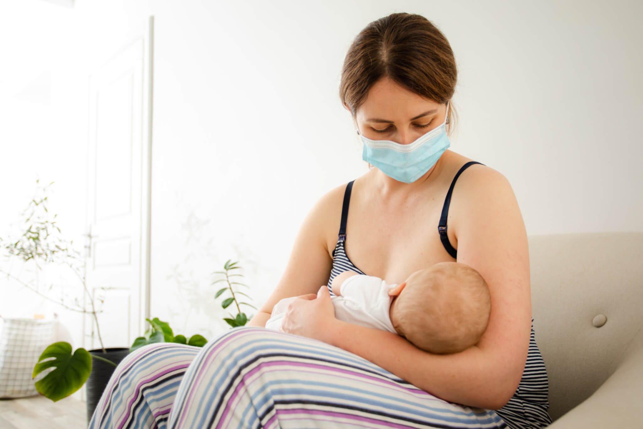 The young mother wearing protective mask while breastfeeding her newborn baby