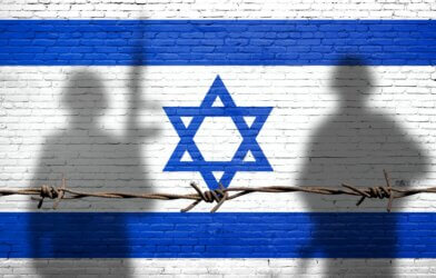Flag of Israel painted on the brick wall with soldiers shadows.