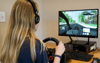teen girl at use a virtual driving assessment program with steering wheel and computer monitor