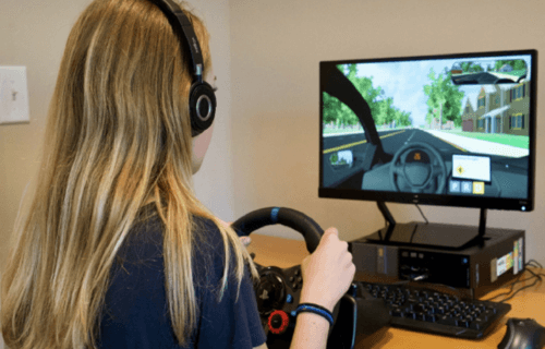 teen girl at use a virtual driving assessment program with steering wheel and computer monitor