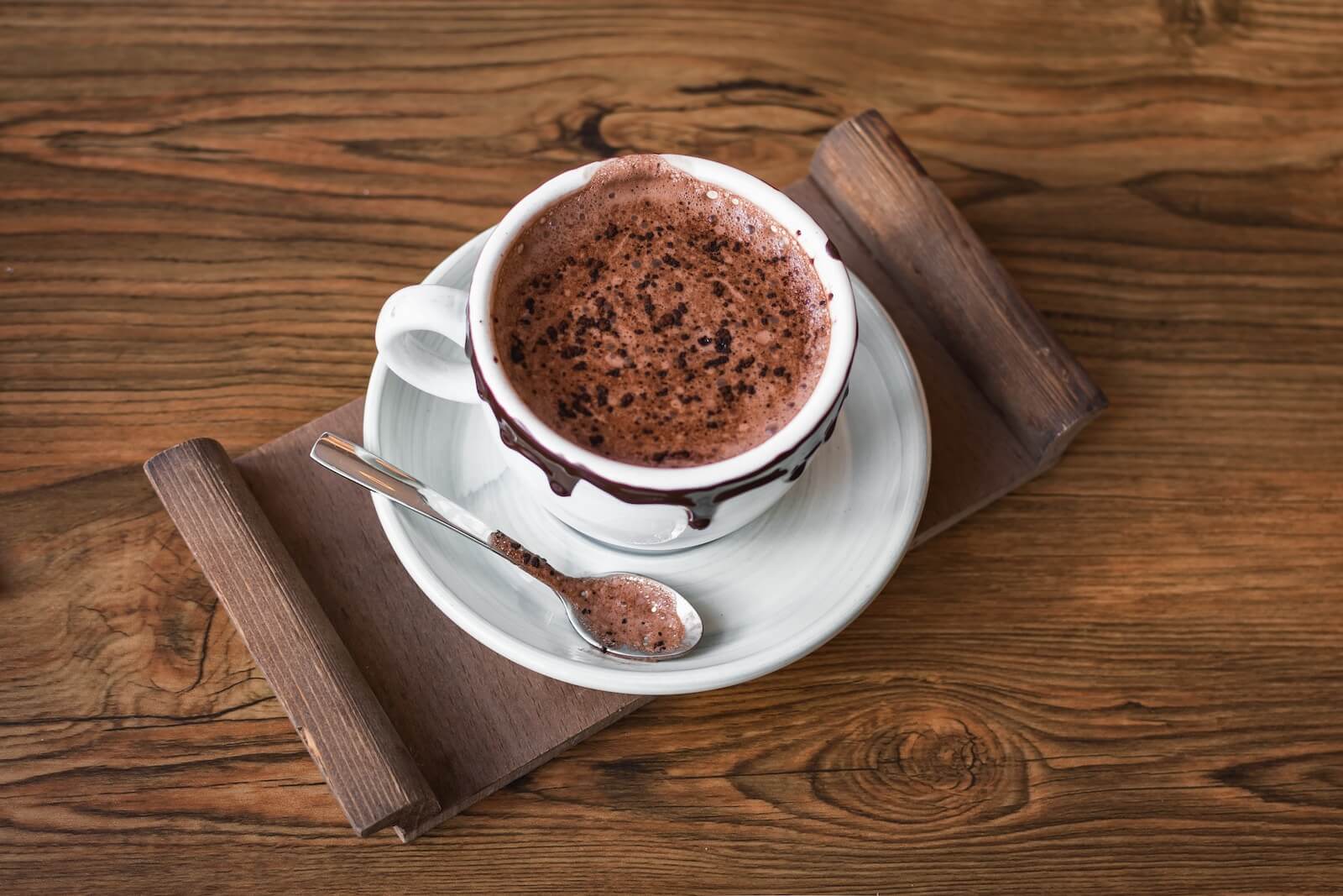 Hot chocolate on saucer with teaspoon on tray.