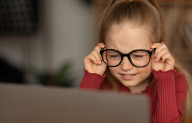 Little girl in glasses struggling with vision while looking at computer
