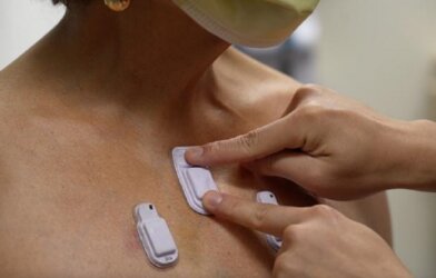 A health care worker places the wearable devices across a patient's chest to capture sounds throughout the lungs that are associated with breathing.