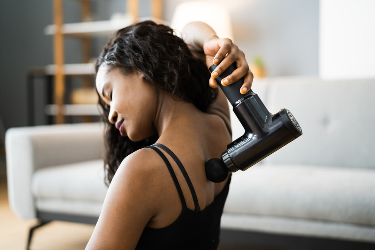 A woman massaging her back with a massage gun