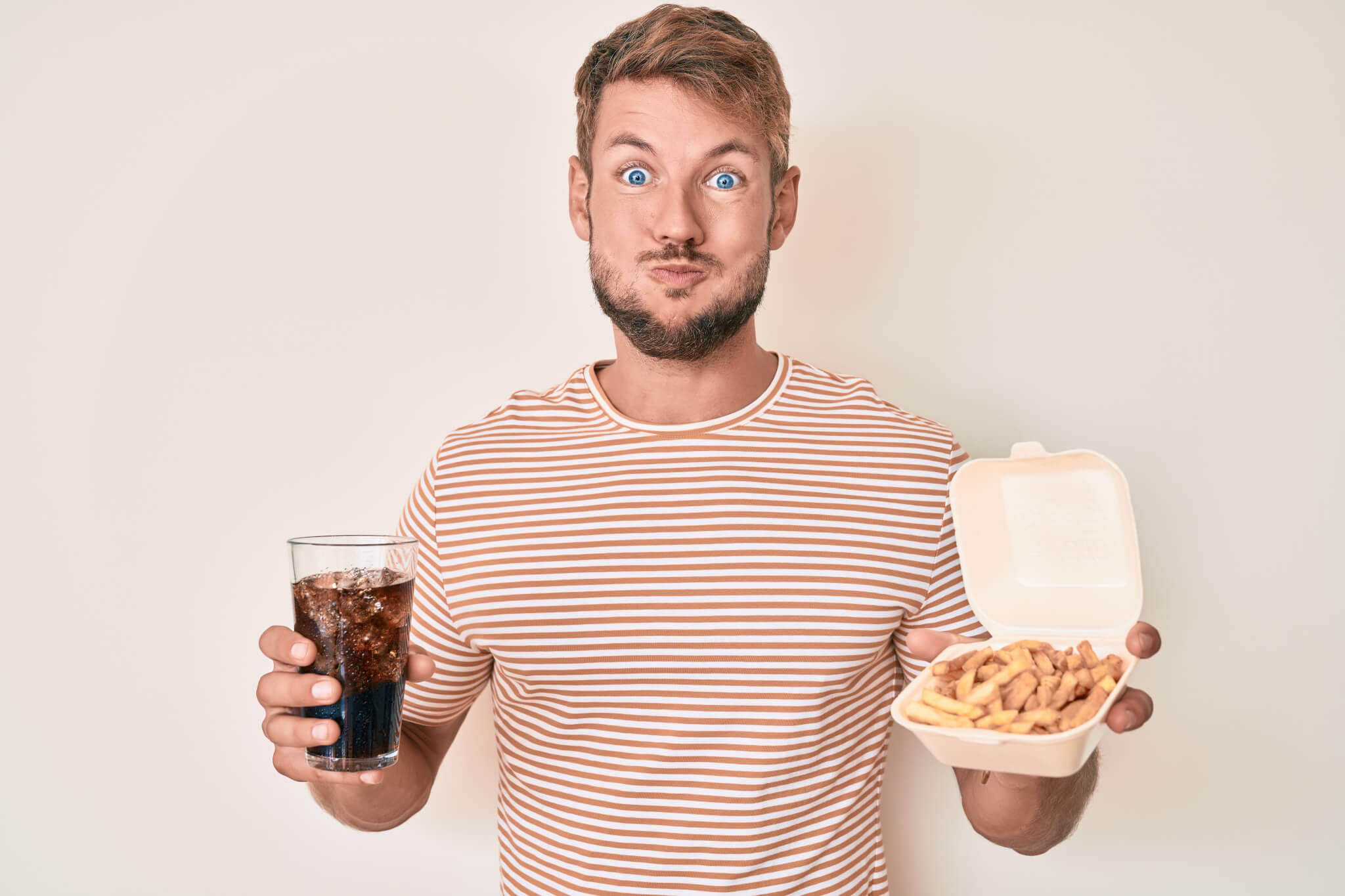 Young man mouth full of food holding soda