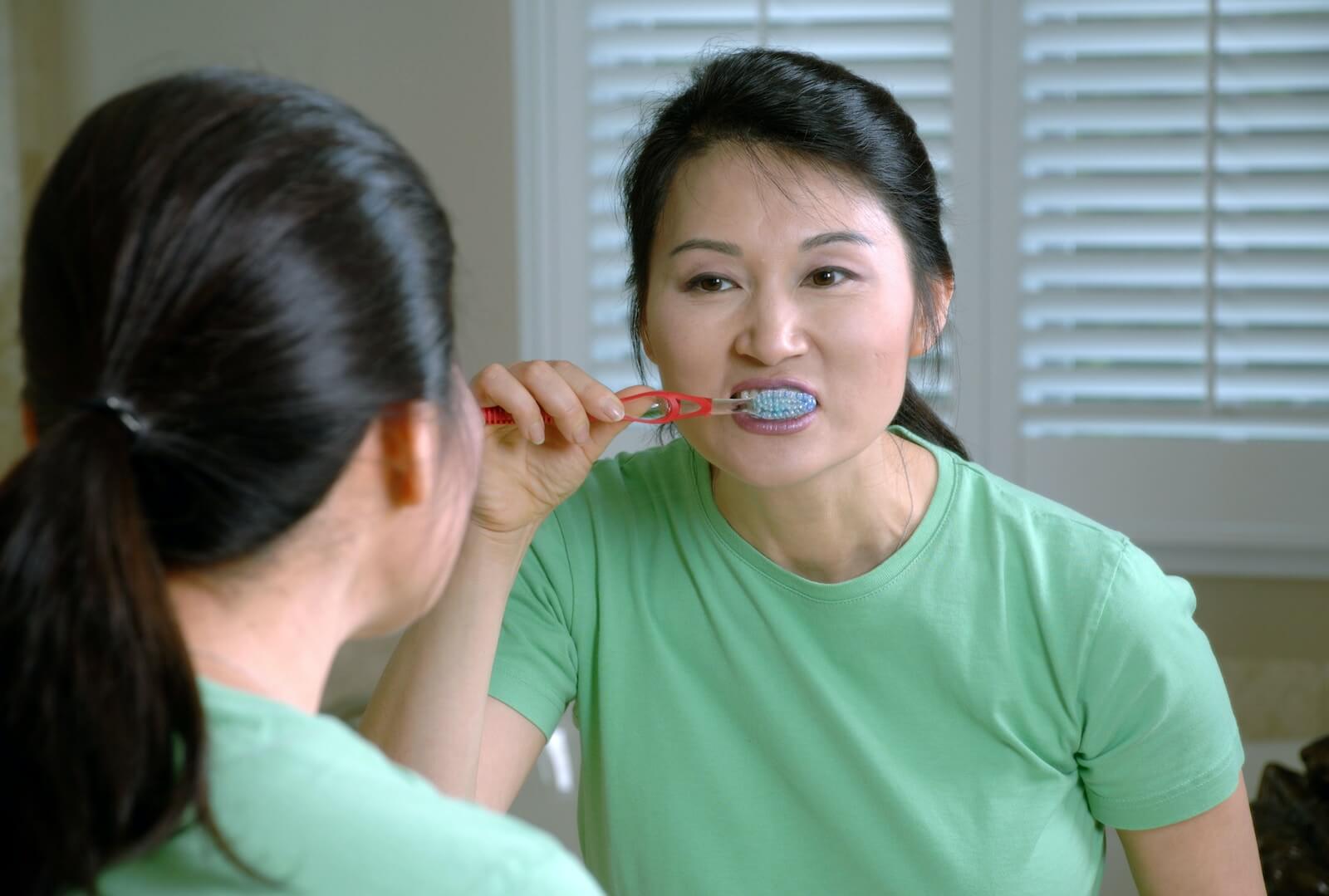 Woman in green crew neck brushing teeth
