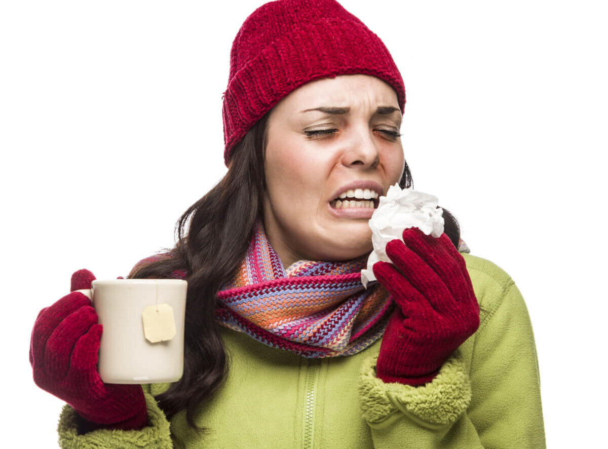 A sick woman drinking tea and sneezing