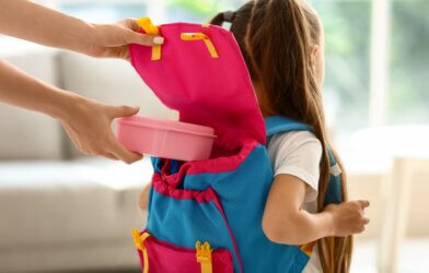 A mother putting school lunch in daughter's backpack