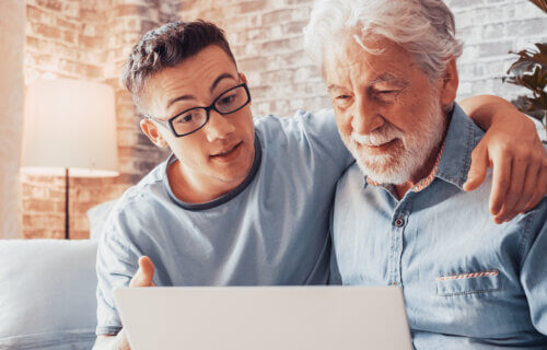 young man helping senior grandfather browse with laptop