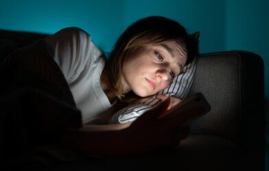Sad woman in bed looking at smartphone