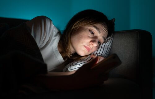 Sad woman in bed looking at smartphone