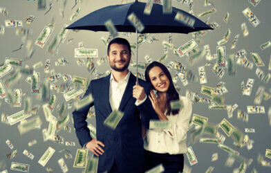 couple with umbrella standing under money rain
