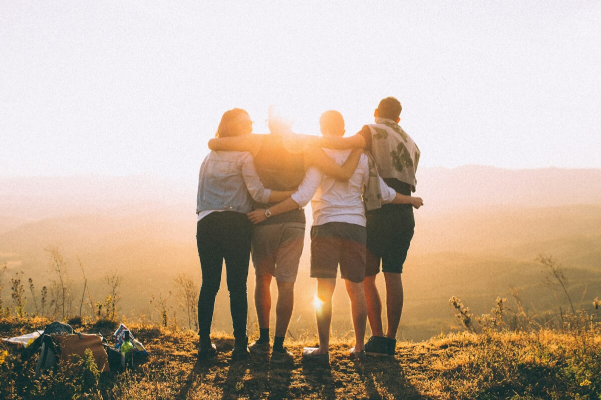 four people stand together with their arms around each other at sunset
