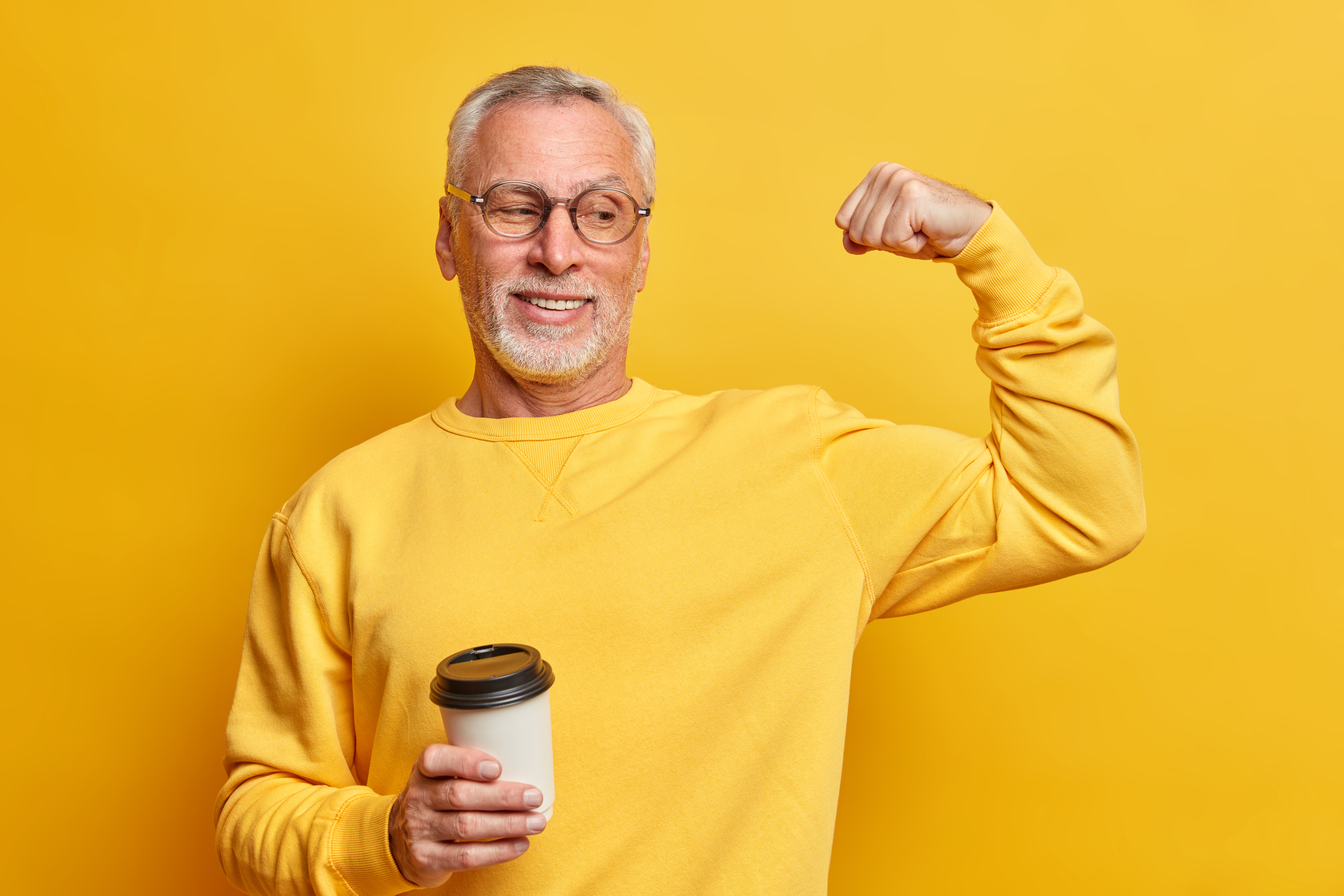 Older man flexing his muscle while drinking coffee