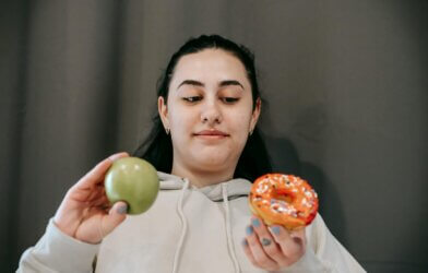 A woman choosing between a donut and an apple