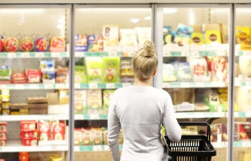 Woman choosing frozen food from a supermarket freezer, reading product information
