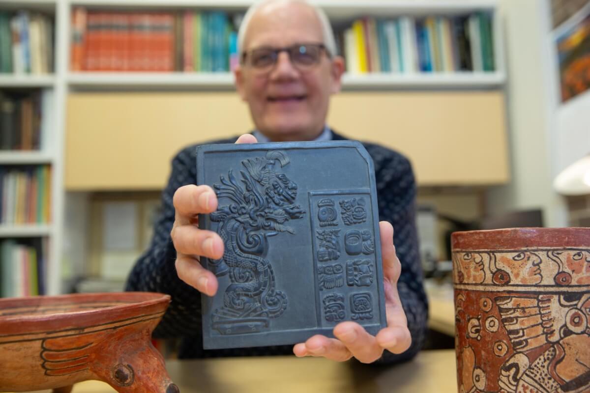 UC Professor David Lentz holds up a sculpture that bears reproductions of ancient Maya glyphs.