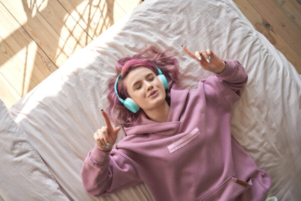 Teen or young woman listening to music on her bed through headphones