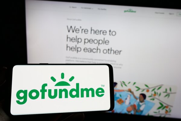 Person holding cellphone with logo of crowdfunding platform company GoFundMe on screen in front of business webpage.